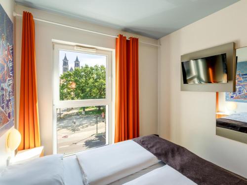 马格德堡B&B HOTEL Magdeburg-City的一间卧室设有大窗户和橙色窗帘