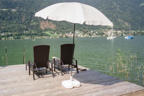 安嫩海姆Seevilla Lotte Ossiachersee的两把椅子坐在带雨伞的码头上