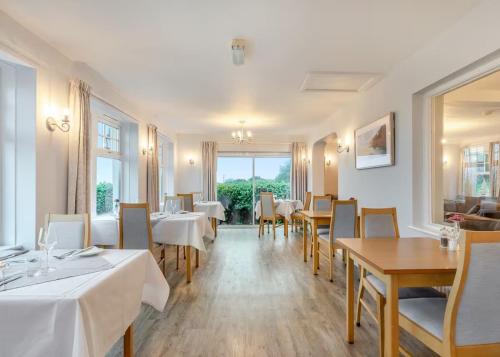 圣阿格尼丝Beacon Country House Hotel & Luxury Shepherd Huts的餐厅设有白色的桌椅和窗户。