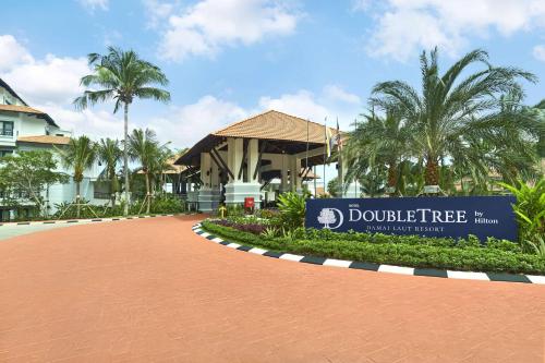 卢穆特DoubleTree by Hilton Damai Laut的棕榈树建筑前的标志