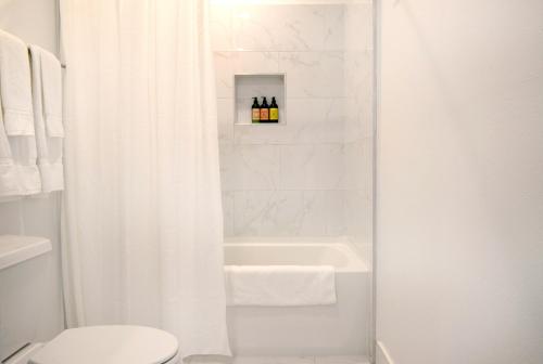 洛杉矶Hollywood Hills Hotel的浴室设有白色的淋浴帘、浴缸和卫生间。