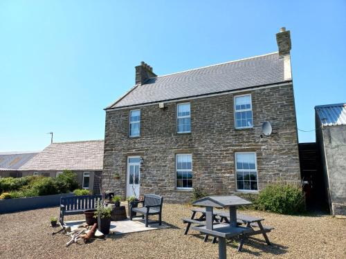 SandayOrkney Retreats 1 2 and 3 bedroom Island Farmhouses & Cottages的砖砌的建筑,前面设有野餐桌和长凳