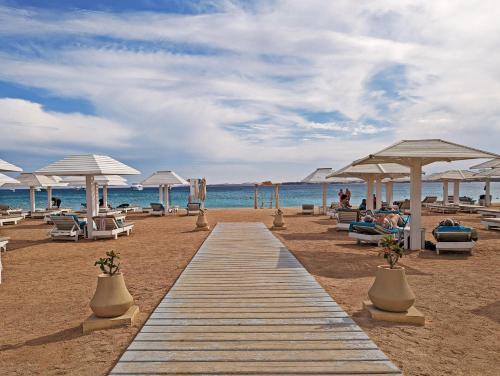 赫尔格达KaiSol Romance Resort Sahl Hasheesh - Adults Only的海滩上的木板路,配有椅子和遮阳伞