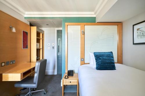 伦敦Thistle London Park Lane的一间卧室配有书桌和一张带蓝色枕头的床