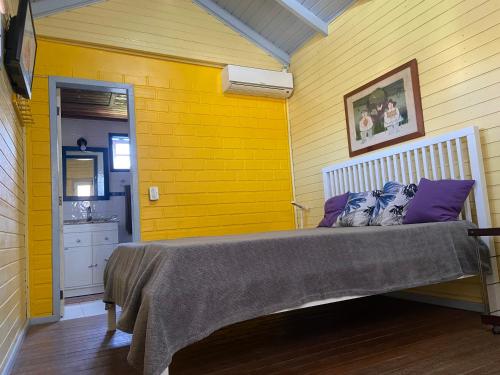 瓜尔达恩巴Casa Guarda do Embaú的一间卧室设有黄色墙壁和一张带紫色枕头的床
