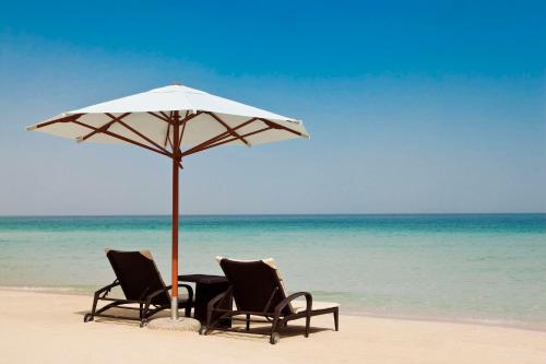 迪拜迪拜朱美拉希尔顿度假酒店的海滩上两把椅子和一张遮阳伞下的桌子