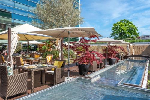 日内瓦Hilton Geneva Hotel and Conference Centre的游泳池旁设有桌子和遮阳伞的游泳池