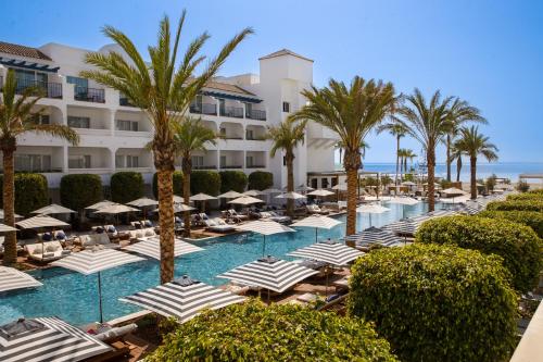 EsteponaMETT Hotel & Beach Resort Marbella Estepona的一个带遮阳伞和棕榈树的游泳池的度假酒店
