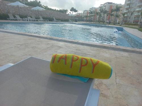 蓬塔卡纳Pool Breeze 202的坐在游泳池旁的黄色木筏,上面写着快乐的