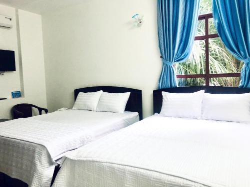 Xa Dau GiayGreen Ville Hotel Đồng Nai的配有蓝色窗帘和窗户的客房内的两张床
