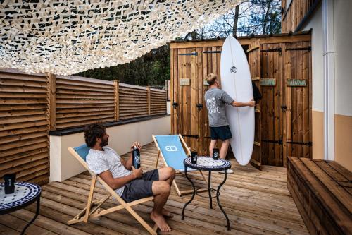 拉卡诺Magic Surf House的两个人坐在带冲浪板的甲板上的椅子上