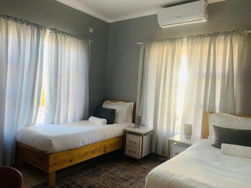 哈博罗内Mmaset Houses bed and breakfast的一间卧室设有两张床,窗户配有窗帘