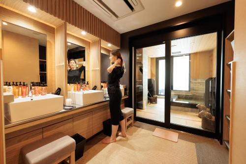 大阪HOTEL Cargo Shinsaibashi的站在浴室镜子前的妇女