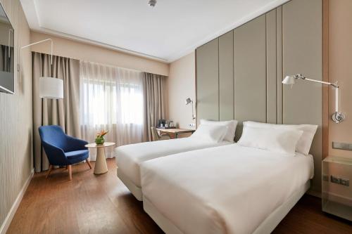 里斯本里斯本格兰德营NH酒店的酒店客房设有一张白色大床和一张蓝色椅子。