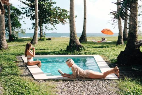 卢纳将军城Punta Punta Surf Retreat的两个女人坐在海滩旁的游泳池旁