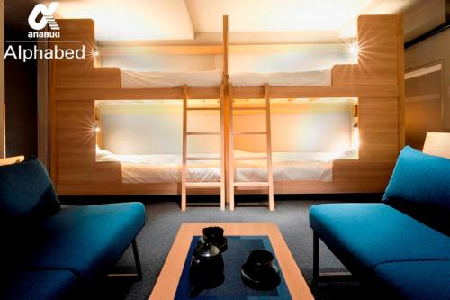 高松ALPHABED INN Takamatsuekimae的客房设有双层床、两把椅子和一张桌子。