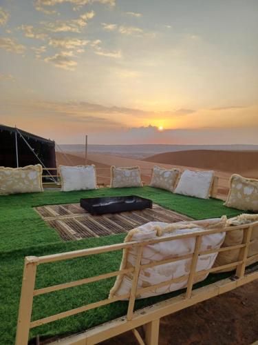 BadīyahSunrise Desert Local Private Camp的沙漠中的一张床铺,背景是日落
