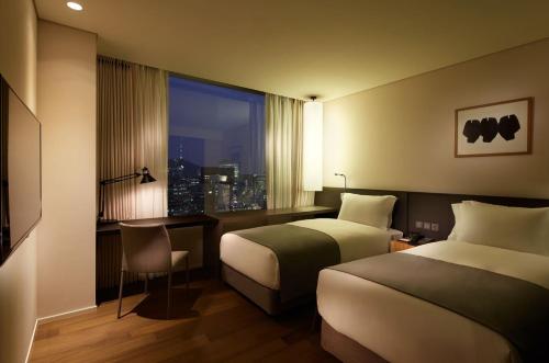 首尔Shilla Stay Mapo Hongdae的酒店客房设有两张床、一张书桌和一个窗户。