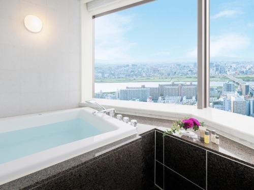 大阪Hotel Hankyu International的带浴缸的浴室和大窗户