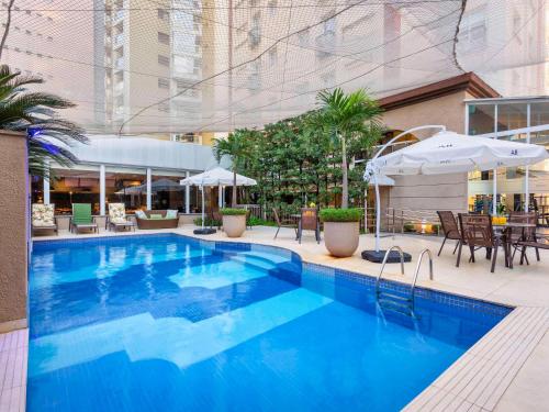 圣保罗圣保罗JK美居酒店的一个带桌子和遮阳伞的大型蓝色游泳池