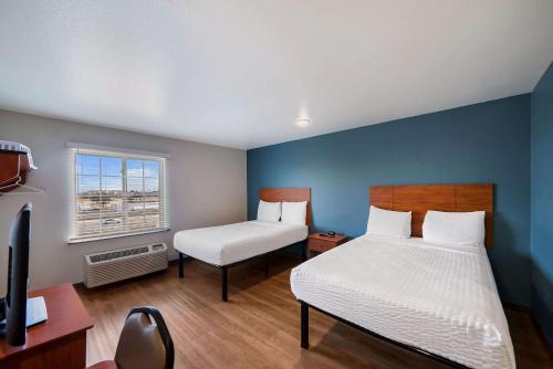 沃思堡WoodSpring Suites Fort Worth Fossil Creek的一间卧室配有两张床、一张桌子和一台电视。