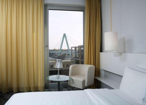 科隆art'otel cologne, Powered by Radisson Hotels的酒店的客房 - 带一张床、椅子和窗户
