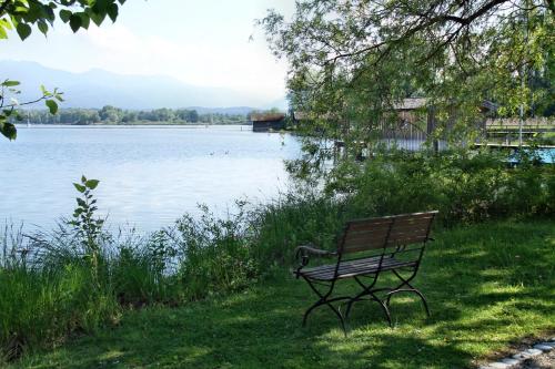 里姆斯廷格Hotel Aiterbach am Chiemsee的坐在湖边草地上的公园长凳