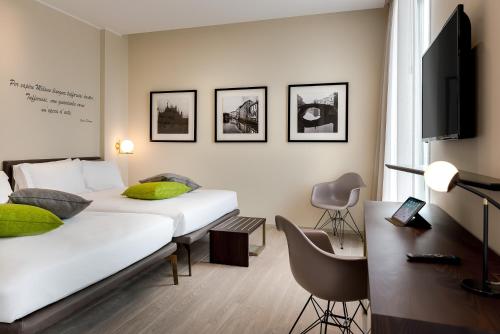 米兰加拿大酒店的一间卧室配有两张床、一张桌子和一台电视。