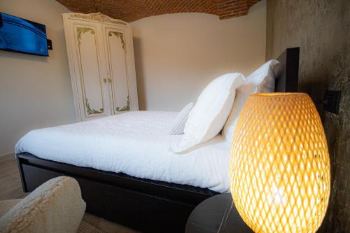伊夫雷亚Le camere del Cappello Verde的一间卧室配有一张带白色床单和一盏灯的床。