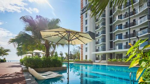 关丹Timurbay Seafront Residences by Nature Home的一座带遮阳伞的游泳池位于大楼旁
