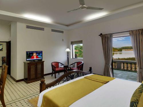 果阿旧城Mercure Goa Devaaya Resort的一间卧室配有一张床、一台电视和一个阳台