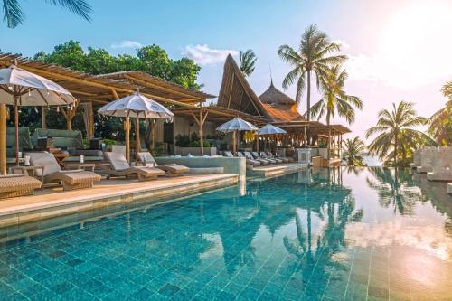 勒吉安巴厘曼迪拉海滩Spa度假酒店的度假村的游泳池,配有椅子和遮阳伞