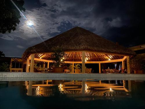 卢甘维尔Hotel Santo Vanuatu的一座带茅草屋顶的建筑,晚上在游泳池旁边