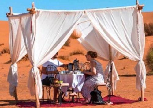 梅尔祖卡Fantastic Luxury Camp的坐在沙漠桌子上的女人