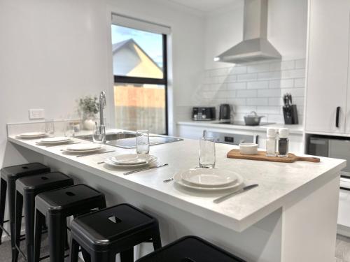 汉密尔顿Villa in Central Hamilton - By KOSH BNB的白色的厨房,厨房里设有台面,上面有凳子和盘子