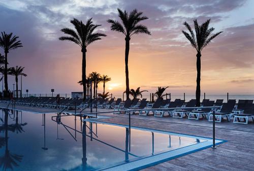 滨海罗克塔斯萨比纳尔最佳酒店的日落时分带棕榈树和椅子的游泳池