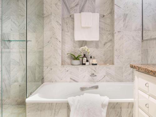悉尼The Sebel Quay West Suites Sydney的浴室铺有大理石瓷砖,配有白色浴缸。
