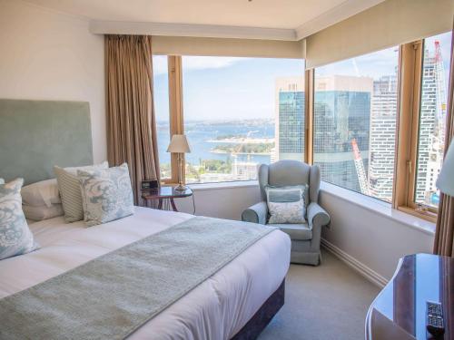 悉尼The Sebel Quay West Suites Sydney的一间卧室配有一张床、一把椅子和一个大窗户