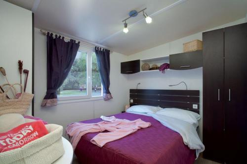 拉戈堡Camping Badiaccia Village的一间卧室配有一张带紫色床单的床和窗户。