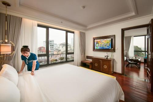 河内San Grand Hotel & Spa的一个小女孩站在酒店房间里的一个床上