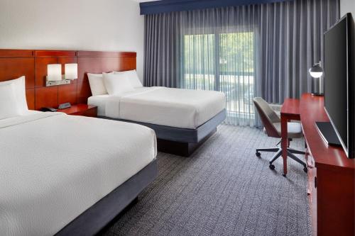 普兰塔寻Courtyard by Marriott Fort Lauderdale Plantation的酒店客房设有两张床、一张桌子和一台电视。