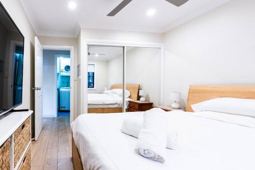 悉尼Funda Place - Leafy Hideout in Northern Beaches的一间白色卧室,配有两张床和电视