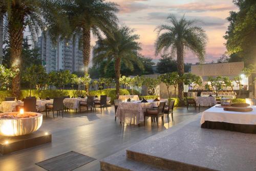 阿格拉阿格拉万怡酒店的一间设有桌椅的餐厅,种植了棕榈树