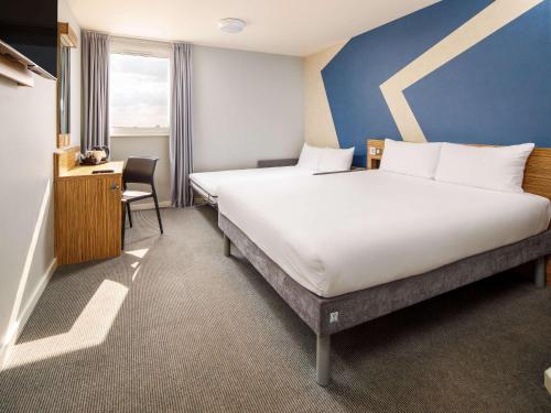 豪士罗ibis budget London Heathrow Central的酒店客房设有一张大床和一张书桌。