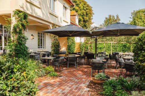 卡布尔Le Castel Cabourg hôtel & SPA- Restaurant La Calypso的一个带桌椅和遮阳伞的庭院