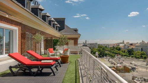 马德里马德里科隆NH系列酒店的阳台配有红色椅子,享有城市美景