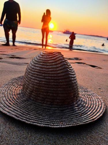 萨尔瓦多Erva Cidreira Hostel的太阳落山时坐在海滩上的一顶草帽