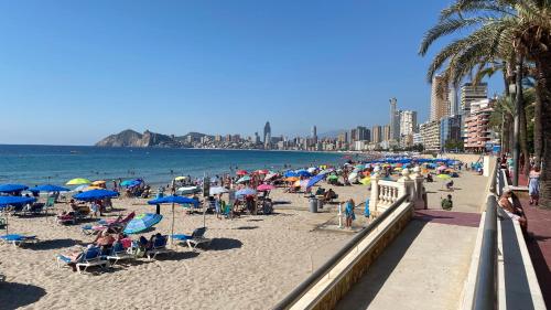 贝尼多姆SOLYMAR PONIENTE Apartamento Recién Reformado A 3 min de Playa Poniente y del Centro Parking Opcional的一群人坐在海滩上,拿着蓝伞