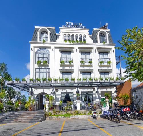 大叻Stillus Boutique Dalat Hotel的一座白色的建筑,前面停有摩托车