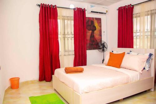AgegeARO (1.0) 2BD Studio Flat (Abule-Egba/Lagos)的一间卧室配有红色窗帘和一张带橙色枕头的白色床。